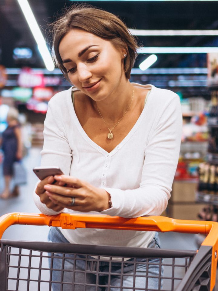 A shopper checking her phone while pushing a cart in a store